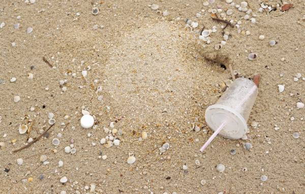 Cannuccia di plastica in un bicchiere di plastica abbonati sulla spiaggia